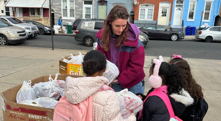 A young woman hands bags of produce to school-aged girls